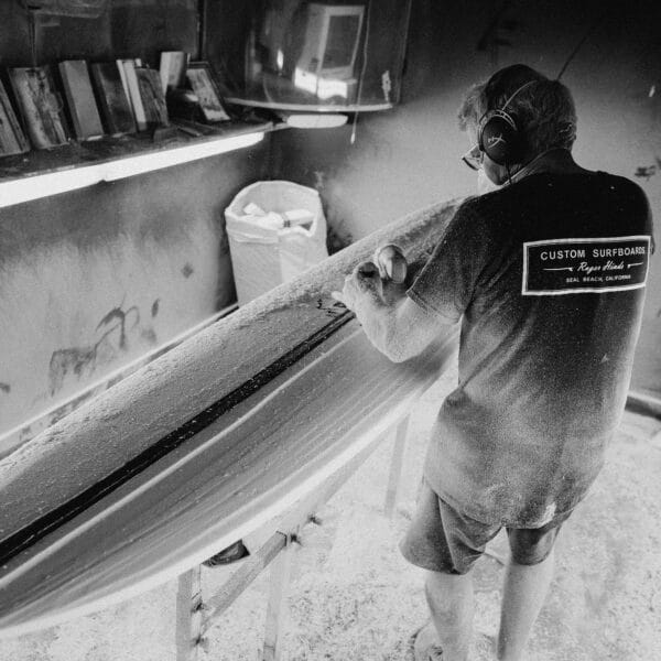 Shapers-Club- Un homme remet à neuf une planche de surf dans un atelier appartenant à Acompte deposite - Roger Hinds. -surfshop-surfboard