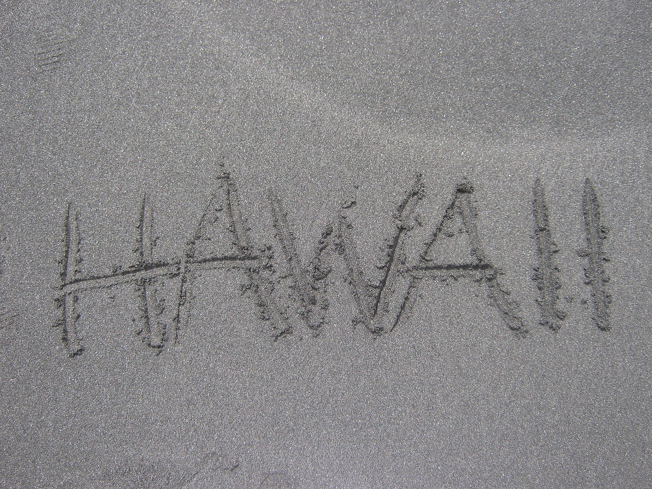 Shapers-Club- Le mot « Hawaii » est écrit à la main en majuscules sur une surface sablonneuse à Sunset Beach. -surfshop-surfboard
