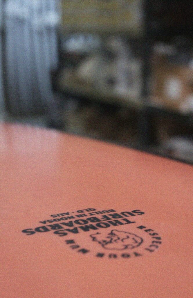 Shapers-Club- Gros plan d'une surface avec un arrière-plan flou, mettant en évidence une empreinte de timbre AUTO-DRAFT avec le texte « passeport chocolat » dans un dessin circulaire. -surfshop-surfboard