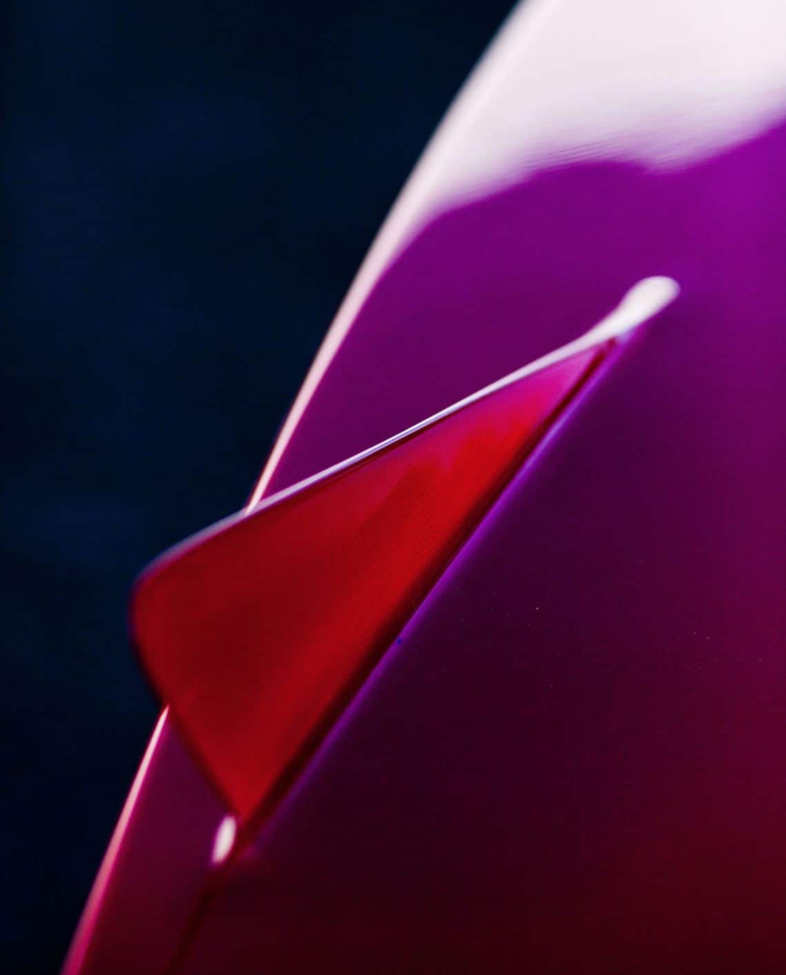 Shapers-Club- Gros plan d'une surface d'aileron de surf, rouge et incurvée se transformant en une zone violette, montrant un contraste saisissant de couleurs avec un accent net sur le bord des ailerons de surf. -surfshop-surfboard